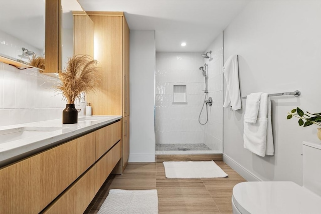 bathroom with a tile shower, toilet, tile patterned flooring, and vanity