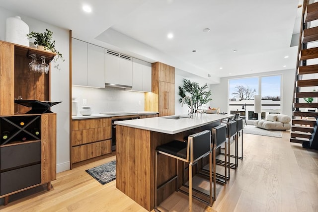 kitchen featuring sink, white cabinets, light wood-type flooring, a kitchen bar, and a kitchen island with sink