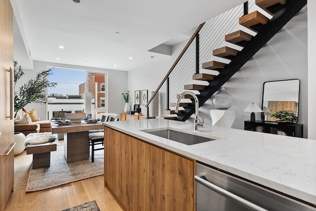 bar featuring sink, light wood-type flooring, light stone counters, and stainless steel dishwasher