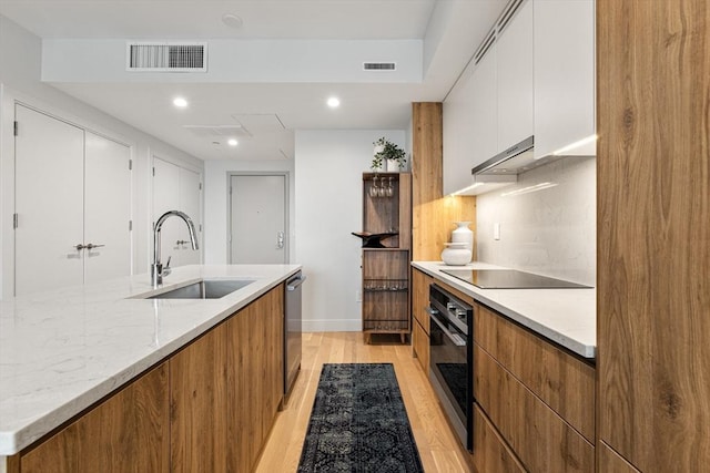 kitchen with wall oven, black electric stovetop, white cabinetry, sink, and light wood-type flooring