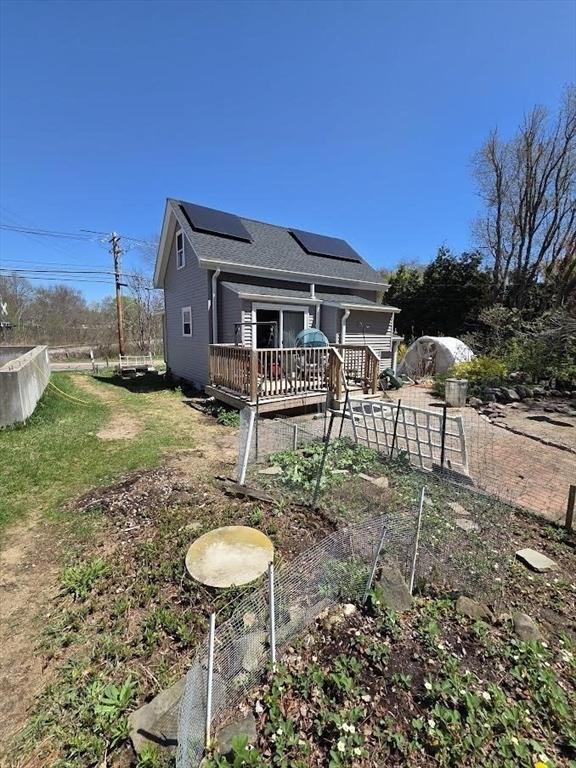 bungalow with a shingled roof, a wooden deck, and roof mounted solar panels