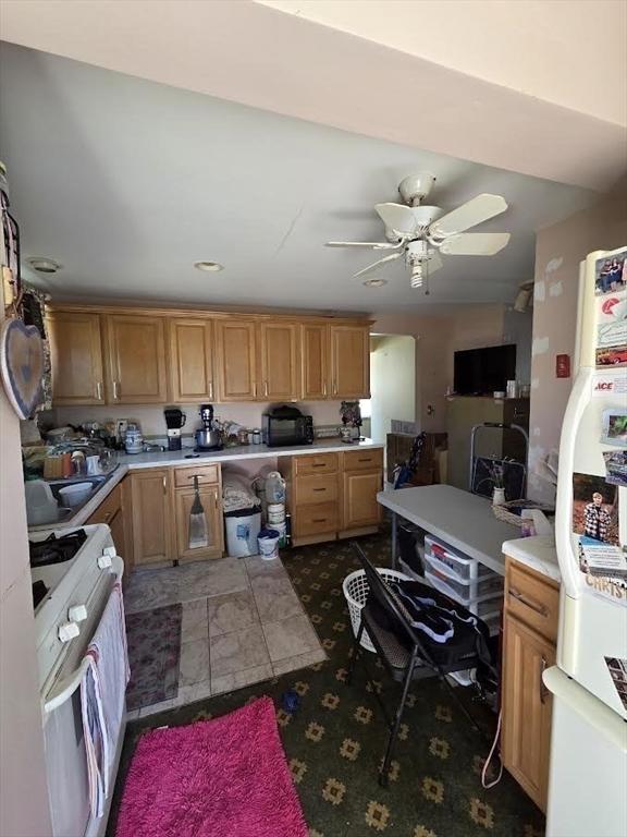 kitchen with a sink, white appliances, light countertops, dark colored carpet, and a ceiling fan