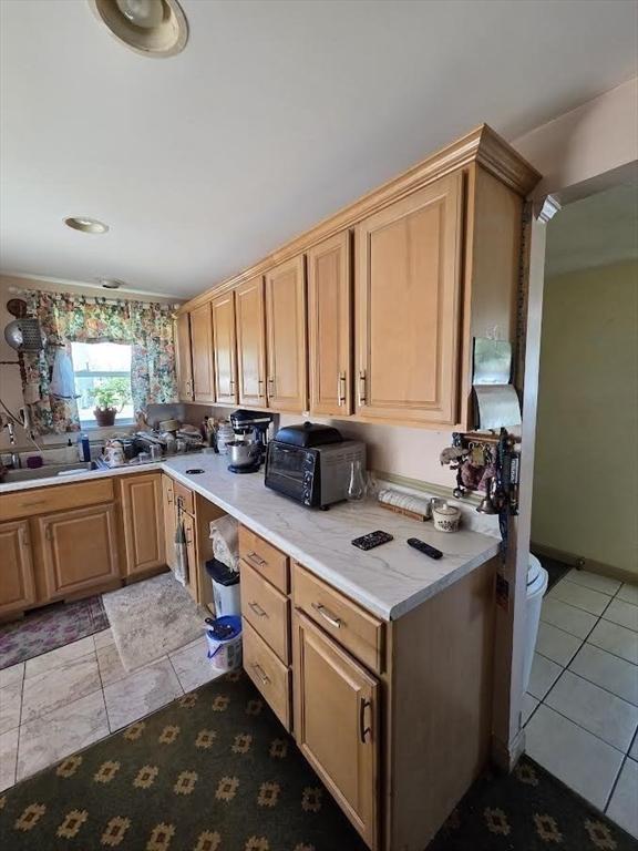 kitchen with a sink, a toaster, light tile patterned flooring, and light countertops