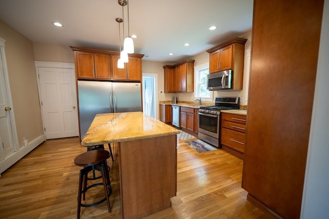 kitchen featuring appliances with stainless steel finishes, a kitchen island, pendant lighting, and light hardwood / wood-style flooring