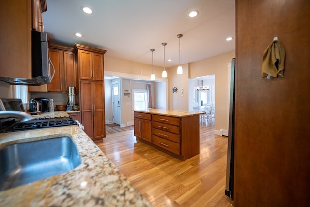 kitchen with pendant lighting, gas range oven, sink, light stone counters, and light wood-type flooring