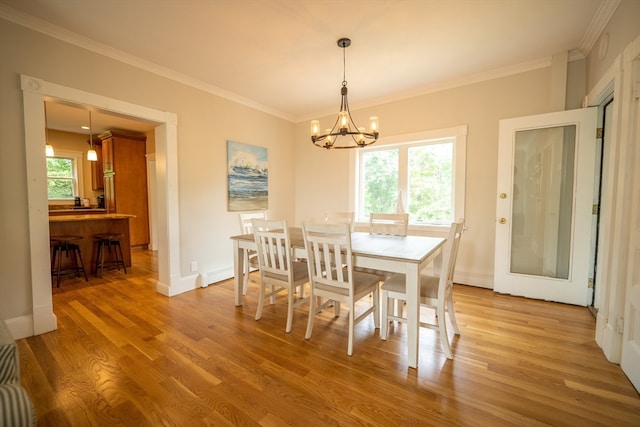 dining space with light wood-type flooring, crown molding, plenty of natural light, and a notable chandelier