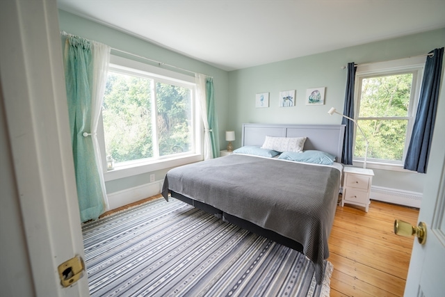 bedroom with light hardwood / wood-style flooring, a baseboard radiator, and multiple windows