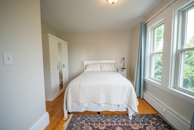 bedroom with baseboard heating, light wood-type flooring, and multiple windows