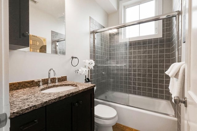 full bath with vanity, bath / shower combo with glass door, and toilet