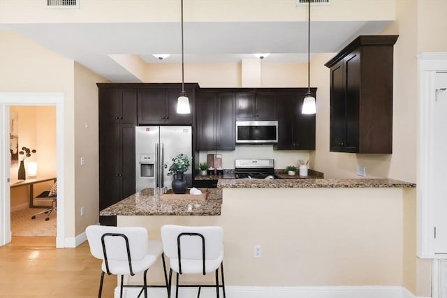 kitchen with stainless steel appliances, light wood-type flooring, a peninsula, stone counters, and pendant lighting