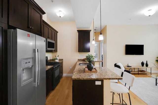 kitchen with stainless steel fridge with ice dispenser, black gas range, a kitchen breakfast bar, light stone countertops, and light wood-type flooring