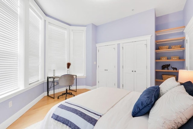 bedroom with two closets, a desk, light wood-type flooring, and baseboards