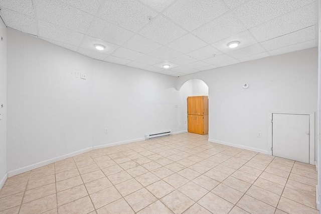 empty room with a drop ceiling, baseboard heating, and light tile patterned floors