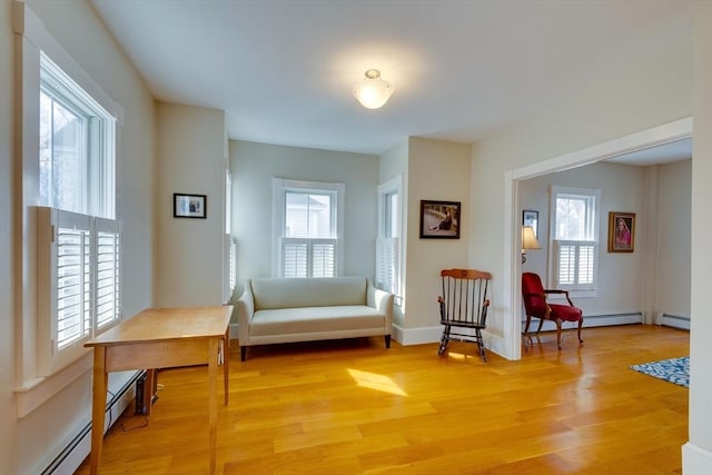 living area with light wood-type flooring, baseboard heating, and a healthy amount of sunlight