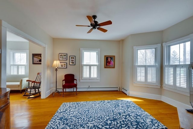 living area with a baseboard heating unit, baseboards, light wood-type flooring, and ceiling fan