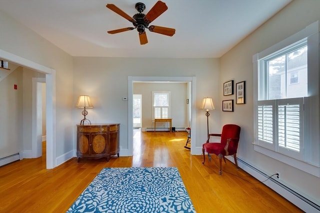 sitting room with a wealth of natural light, a baseboard heating unit, and light wood finished floors