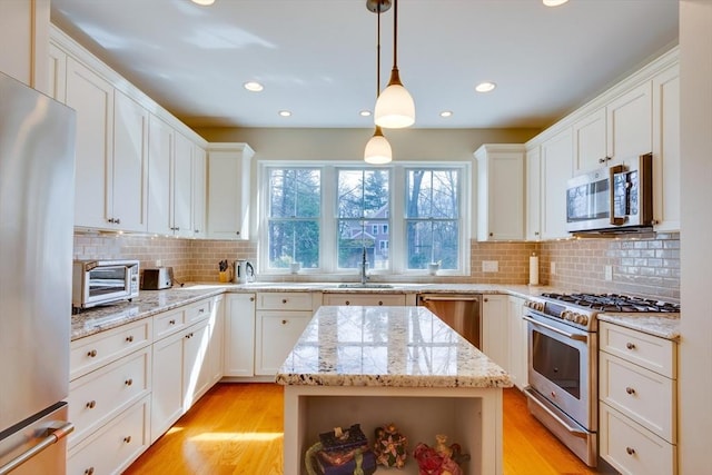 kitchen featuring light wood finished floors, white cabinets, appliances with stainless steel finishes, and a sink