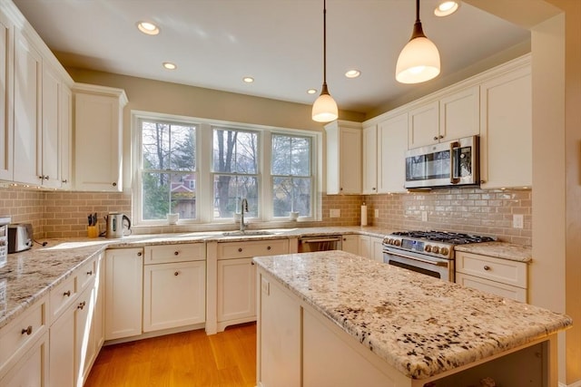 kitchen featuring light stone countertops, a kitchen island, a sink, appliances with stainless steel finishes, and light wood-type flooring