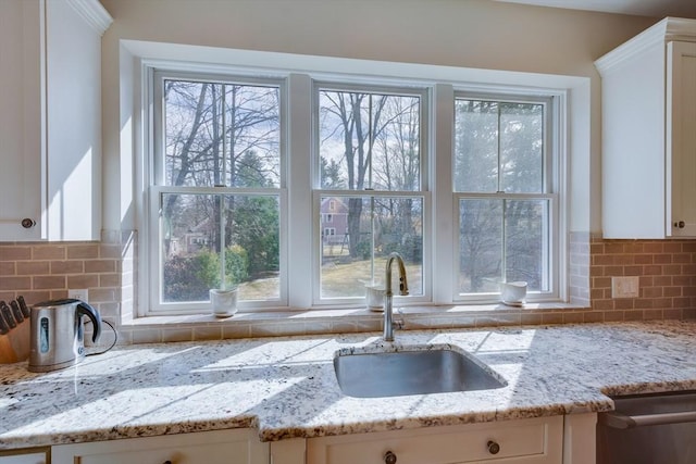 kitchen featuring light stone countertops, a sink, dishwasher, white cabinetry, and tasteful backsplash