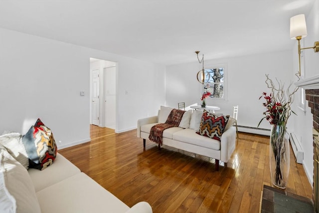 living room with wood-type flooring, a brick fireplace, and a baseboard heating unit