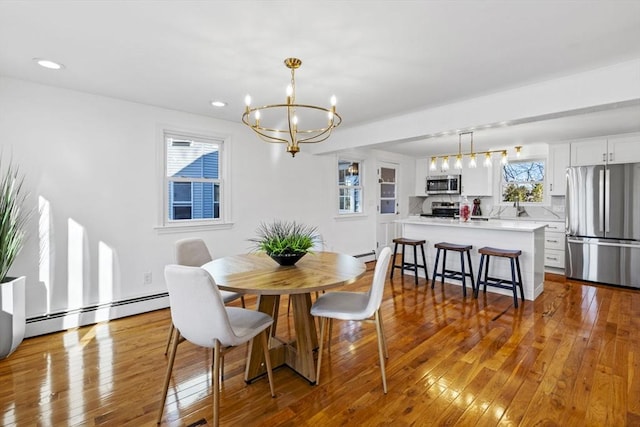 dining space featuring a chandelier, light hardwood / wood-style floors, baseboard heating, and sink