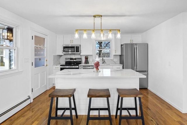 kitchen with a breakfast bar, white cabinets, baseboard heating, a kitchen island, and stainless steel appliances