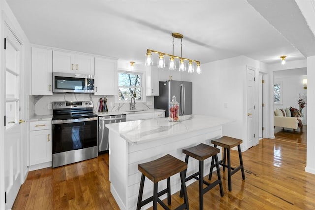 kitchen with decorative backsplash, decorative light fixtures, stainless steel appliances, and white cabinetry