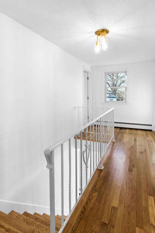 corridor with hardwood / wood-style flooring and a baseboard heating unit