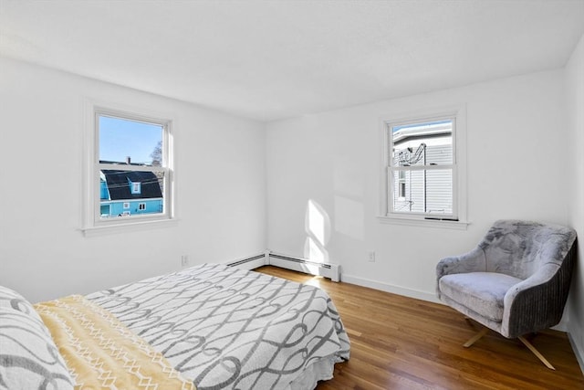 bedroom with multiple windows, hardwood / wood-style floors, and a baseboard heating unit