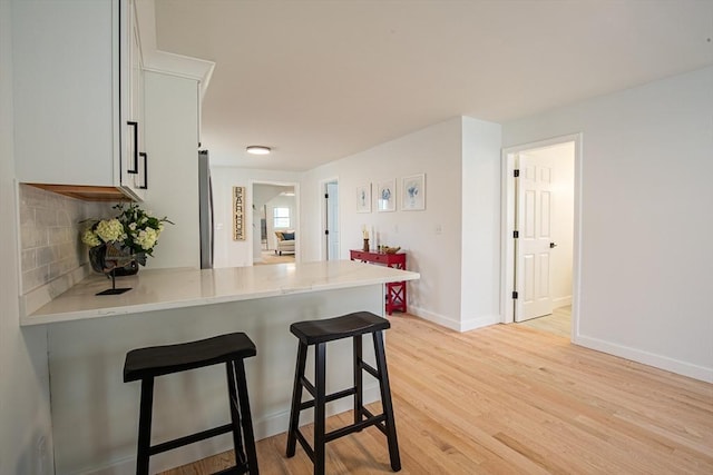 401 N End Blvd, Salisbury, MA 01952 - kitchen with a breakfast bar, a peninsula, light wood-type flooring, white cabinets, and tasteful backsplash