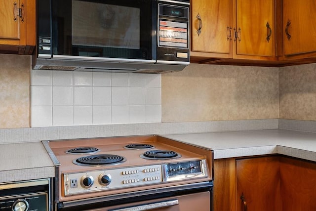 kitchen with black microwave, range with electric stovetop, light countertops, backsplash, and brown cabinets