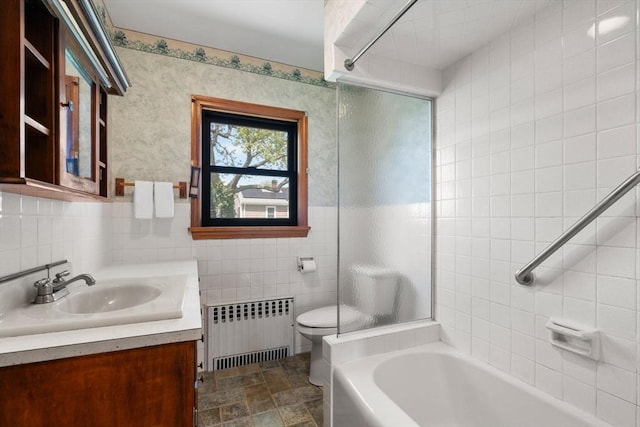 full bath with radiator heating unit, tile walls, toilet, vanity, and stone finish flooring
