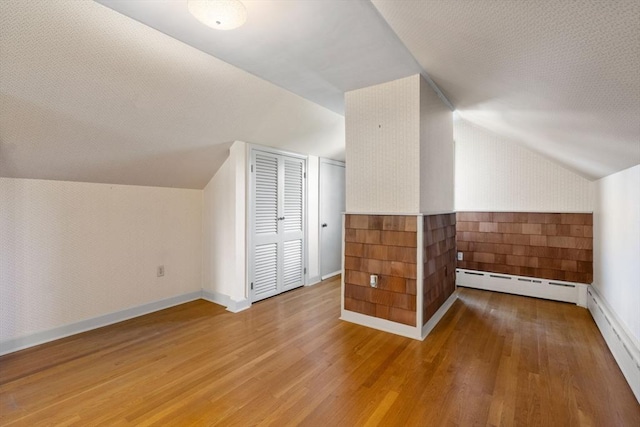 additional living space featuring baseboard heating, wood finished floors, lofted ceiling, and baseboards