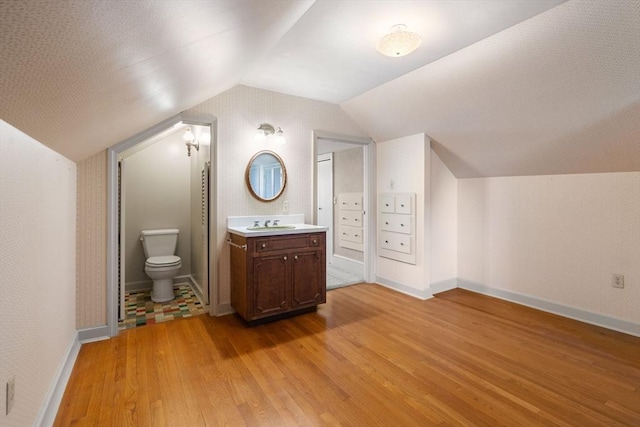 bathroom featuring wood finished floors, toilet, vanity, vaulted ceiling, and baseboards
