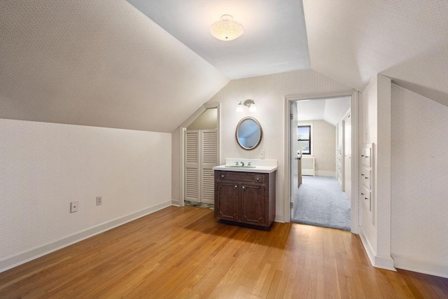 additional living space with light wood-type flooring, a sink, lofted ceiling, and baseboards