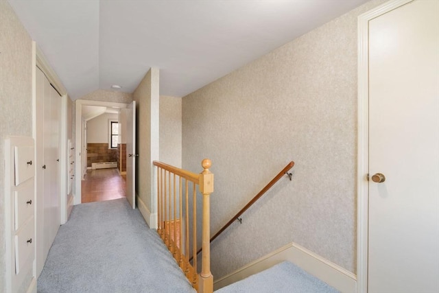 corridor featuring an upstairs landing, vaulted ceiling, a baseboard radiator, and light carpet