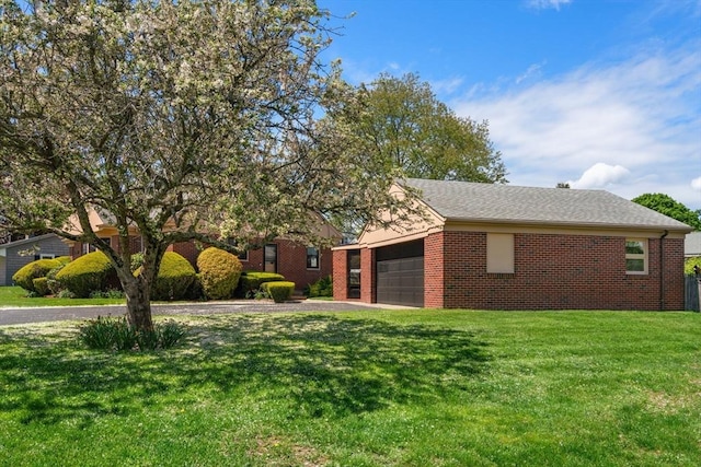 view of front of house featuring an attached garage, a front yard, brick siding, and asphalt driveway