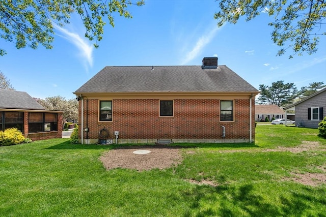 rear view of property featuring a chimney, a yard, roof with shingles, and brick siding