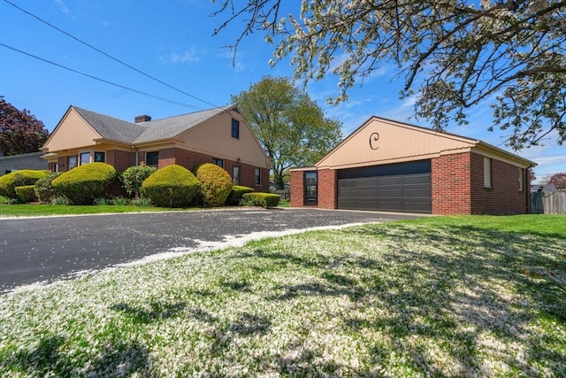 view of side of property featuring brick siding, a lawn, asphalt driveway, an outbuilding, and an attached garage