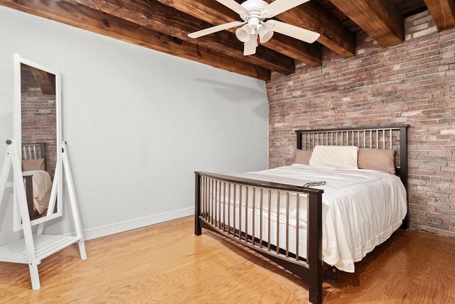 bedroom featuring beam ceiling, brick wall, a ceiling fan, baseboards, and wood finished floors