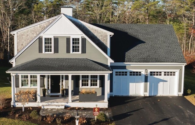 view of front facade featuring a shingled roof, a porch, a chimney, a garage, and driveway