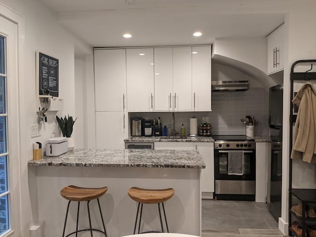 kitchen with stainless steel electric range, a sink, a peninsula, a breakfast bar area, and white cabinetry