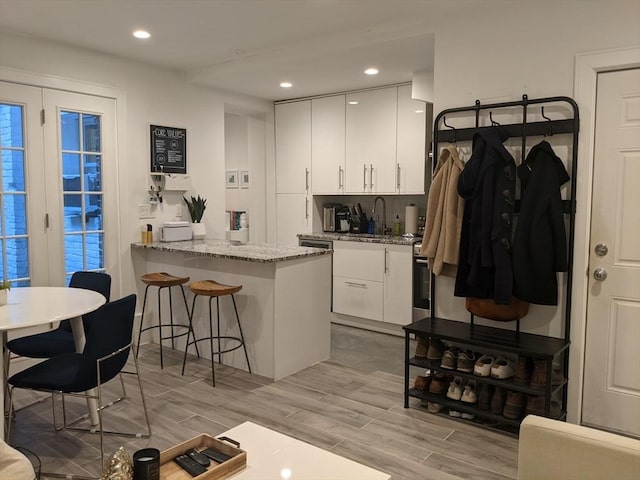 kitchen with a sink, white cabinets, light wood-type flooring, a breakfast bar, and light stone counters