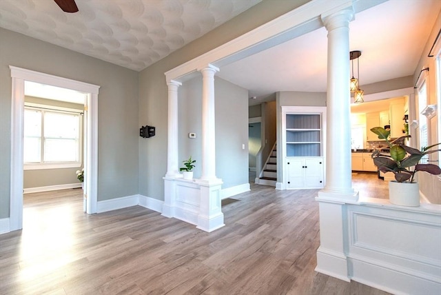 interior space featuring light wood-style floors, decorative columns, stairway, and baseboards