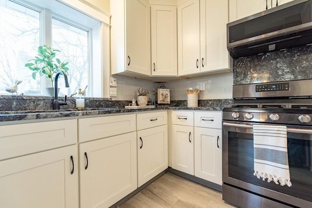 kitchen with light wood finished floors, white cabinets, dark stone counters, appliances with stainless steel finishes, and backsplash