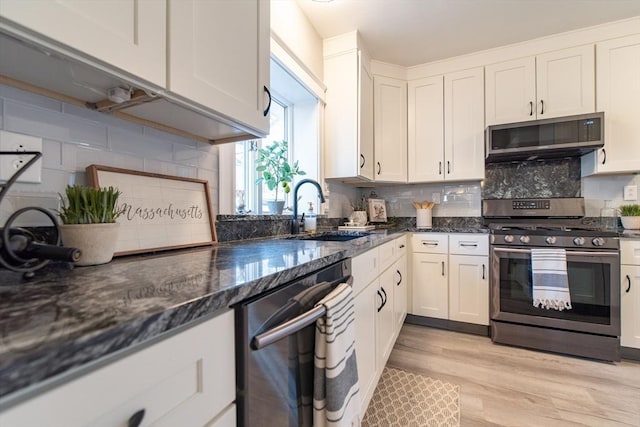 kitchen featuring light wood-style flooring, a sink, appliances with stainless steel finishes, tasteful backsplash, and dark stone countertops