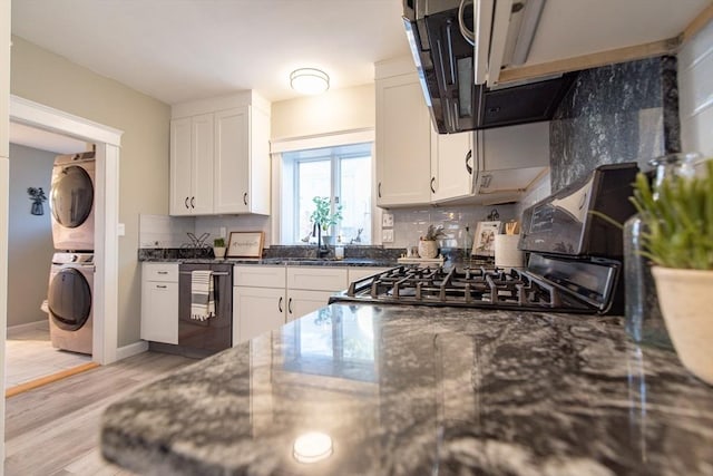 kitchen with stacked washer and dryer, white cabinets, light wood-style floors, and dishwashing machine