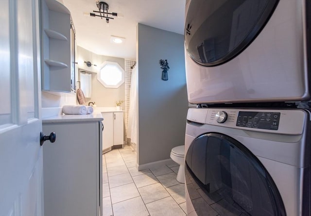 laundry area featuring stacked washer and dryer, laundry area, light tile patterned flooring, and baseboards