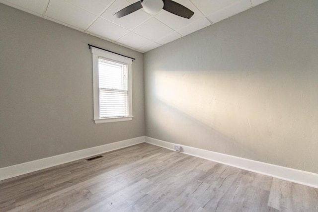 unfurnished room featuring baseboards, visible vents, a drop ceiling, and wood finished floors