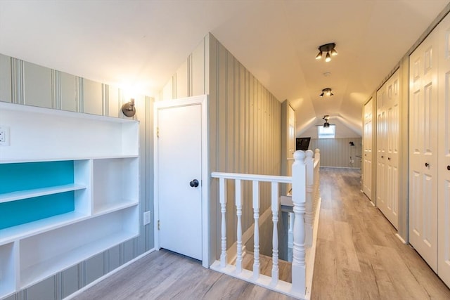 corridor with lofted ceiling, light wood-style floors, built in shelves, and an upstairs landing